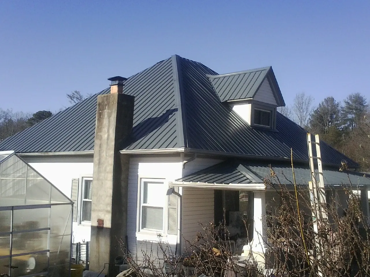 Dark blue standing seam metal roof on a white farmhouse with dormer — Slate & Tile Roof Repair by Roofing Brothers in Northbrook