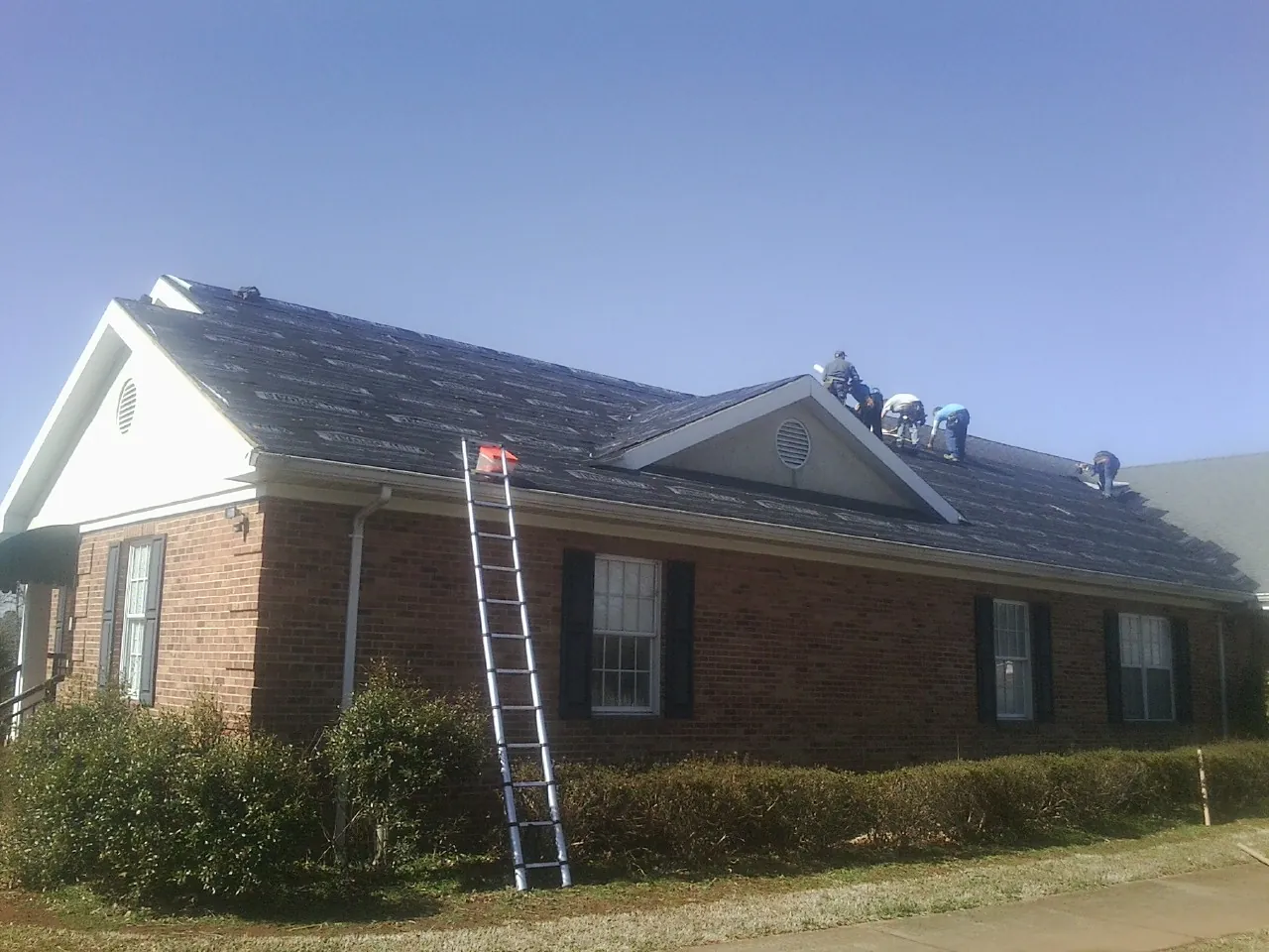 Crew tearing shingles off a brick ranch roof with a ladder set — Emergency Roof Repair work by our crew in Northbrook