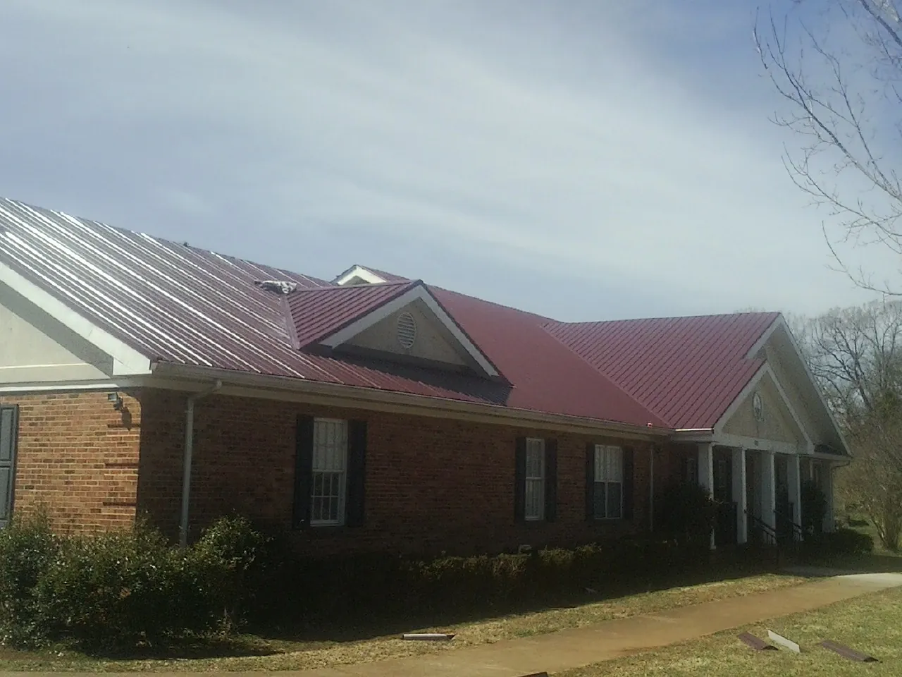 Red metal roof with gabled entries on a long brick building, from a Hail Damage Roof Repair job in Northbrook