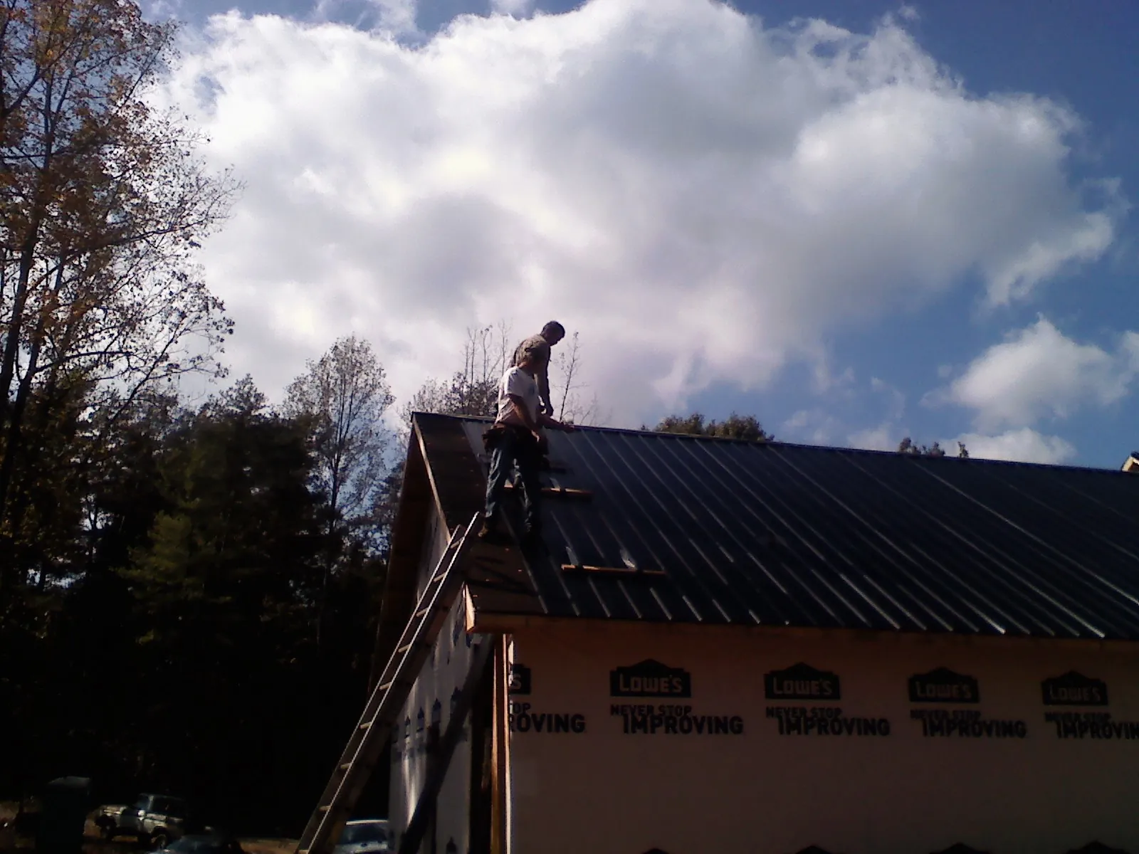 Roofer fastening dark metal panels high against a cloudy sky, from a Roof Inspection job in Northbrook